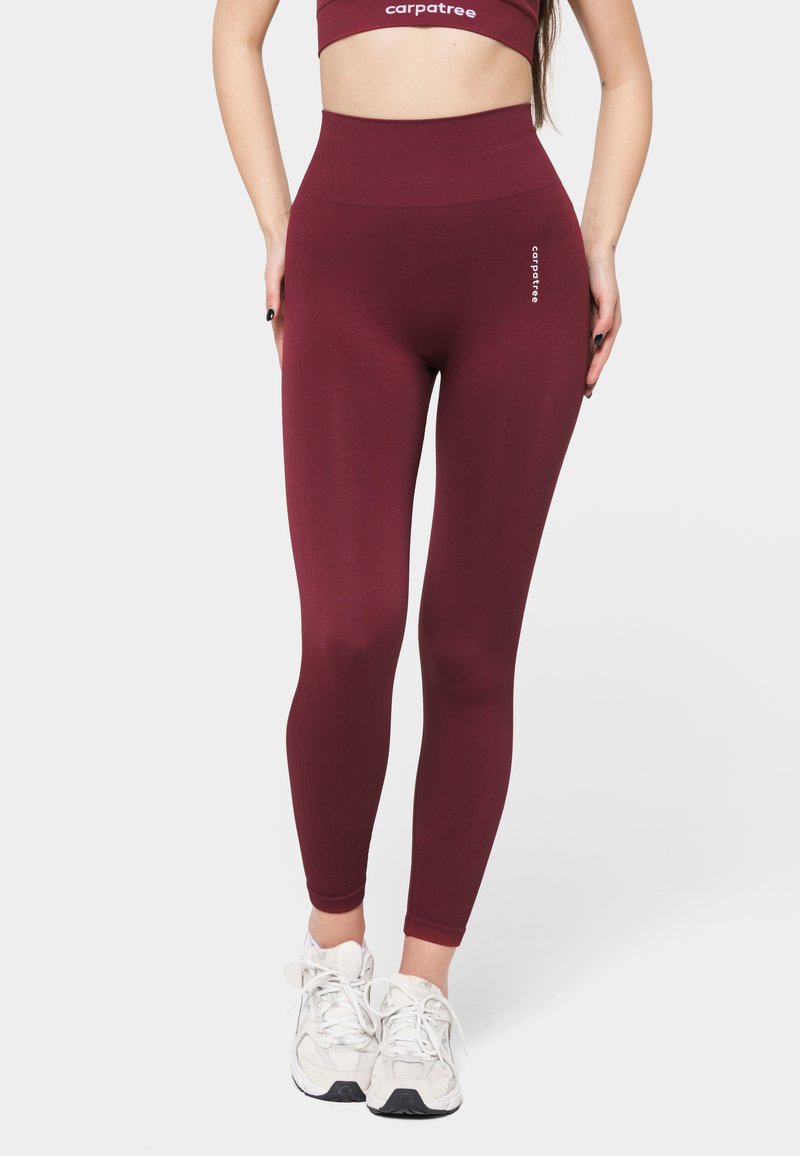 Maroon high-waisted leggings made of stretchy fabric with ribbed texture; features branding on the thigh and paired with white sneakers.