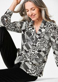 Blusa a fantasia bianco e nero realizzata in tessuto liscio, con chiusura a bottoni sul davanti, maniche lunghe e vestibilità comoda.