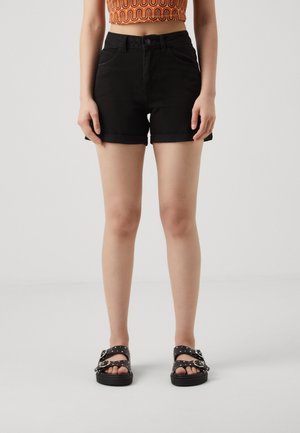 Shorts de mezclilla negra con dobladillo doblado, diseño de cinco bolsillos y cintura alta, combinados con sandalias negras que tienen tachuelas plateadas.
