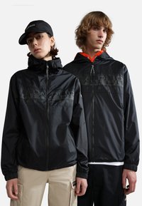 Zwarte lichtgewicht jassen met ritsvoorkant en capuchons, met elastische manchetten. Eén jas heeft oranje accenten en logo-details.