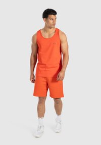 Jasnopomarańczowy podkoszulek na ramiączkach i szorty wykonane z bawełny. Podkoszulek ma małe logo; szorty mają boczną kieszeń i płaski pas.