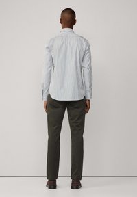 Gestreepte button-up shirt in blauw en wit, met lange mouwen en een gebogen zoom. Gecombineerd met olijfgroene broek en bruine schoenen.