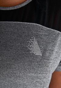 Grå sports T-shirt med struktureret stof. Har et sort afsnit øverst og et geometrisk logo i en lysere grå på brystet.