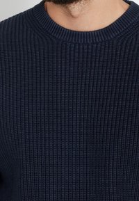 Mörkblå ribbad tröja med rund halsringning och texturerad stickning, med en närbild som visar den fina detaljeringen i tygmönstret.