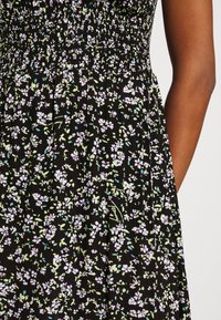 Svart klänning med blommönster i vitt, rosa och grönt. Rynkad kropp och plisserad design som framhäver en lätt tygtextur.