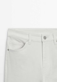 Vue de face d'un jean en denim blanc montrant la taille, la fermeture par bouton, les passants de ceinture et la poche avant gauche avec des rivets.