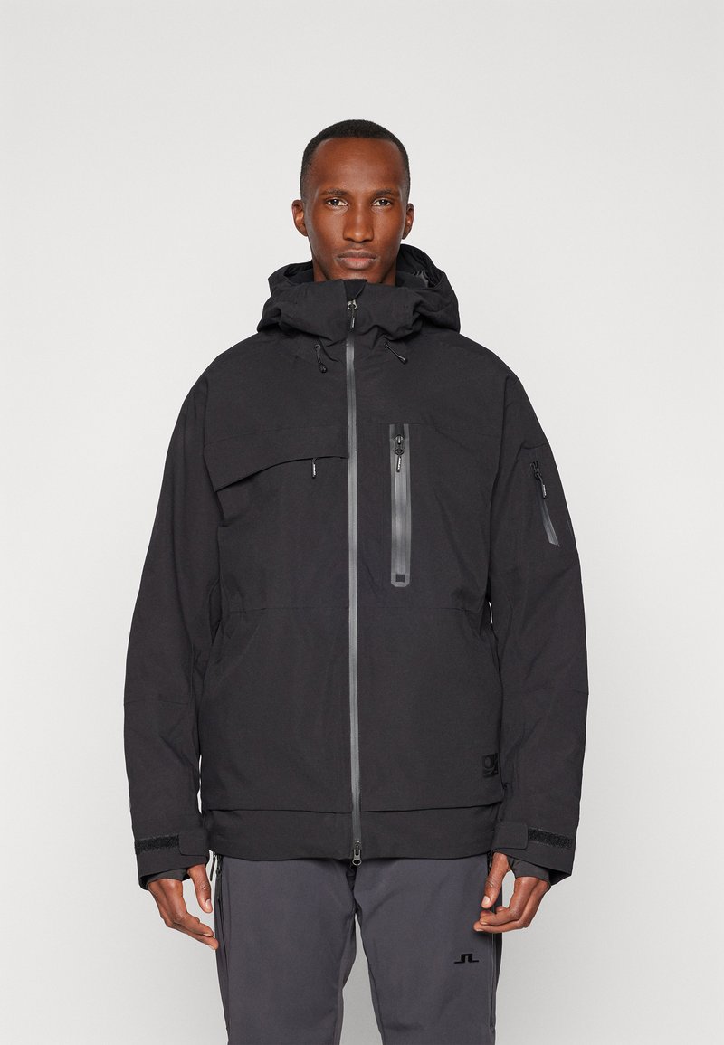 Black waterproof jacket with a hood, front zip closure, multiple zippered pockets, and textured fabric. Features adjustable cuffs and hem.
