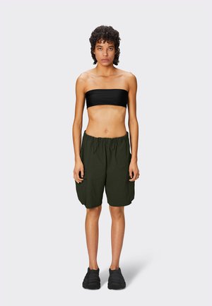 Haut bandeau noir et shorts amples vert olive avec une finition texturée. Le modèle porte des chaussures noires à enfiler, se tenant devant un fond neutre.