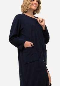 Accappatoio blu navy con zip in morbido tessuto di spugna, dotato di due tasche frontali e una vestibilità comoda, con fessure laterali per facilitarne il movimento.