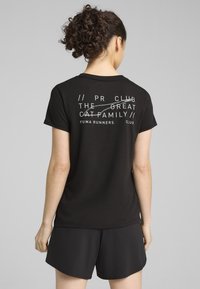 Sort bomulds t-shirt med hvid grafisk tryk på ryggen med tekst, parret med sorte shorts. Designet har en afslappet pasform og korte ærmer.