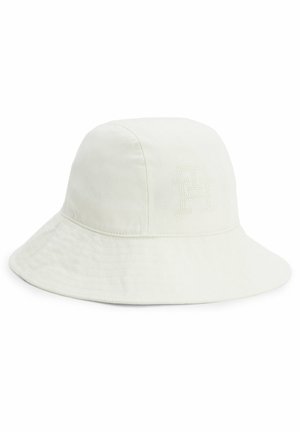 Wyblakły kremowy kapelusz typu bucket wykonany z bawełny, z naszytym logo z przodu i wąskim rondem opadającym do dołu.