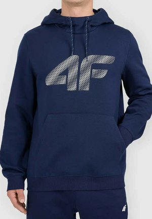 Mann trägt dunkelblauen Hoodie mit weißem strukturiertem 4F-Logo, Kängurutasche und passende dunkelblaue Sweatpants mit kleinem 4F-Logo.