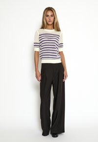 Jersey de punto en crema con rayas moradas y mangas cortas, combinado con pantalones de pierna ancha negros. Textura suave con un corte relajado.