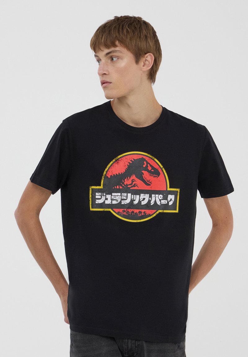 T-shirt di cotone nera con un audace logo di Jurassic Park rosso e giallo, centrato sul davanti, con una grafica di dinosauro e testo giapponese.