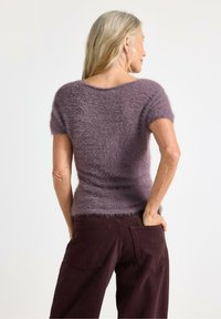 Lilla, fuzzy sweater med korte ærmer og rund hals, båret med mørk burgunder bukser. Blød tekstur og tætsiddende design.