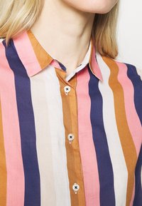 Randig skjorta med knapp-up i rosa, orange, vitt och marinblått. Har krage och svarta knappar längs den främre placket.