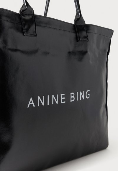 Sac fourre-tout noir avec des poignées brillantes et "ANINE BING" imprimé en lettres capitales blanches sur le devant.