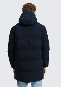 Cappotto imbottito blu navy con cappuccio, dotato di un design trapuntato e di un taglio più lungo, realizzato in un materiale liscio e leggero.