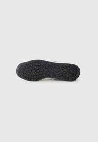 Suola di sneaker in gomma nera con vari nibbii arrotondati per la trazione. Parte superiore di colore crema con accenti blu. Design semplice e funzionale.