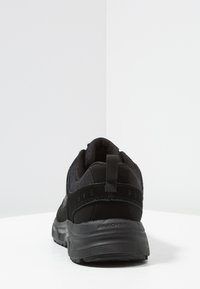 Černá sportovní obuv s vrchní částí z prodyšné síťoviny a semiše, zaoblenou špičkou, polstrovaným límcem a texturovanou gumovou podrážkou; obsahuje zadní poutek pro snadné obouvání.