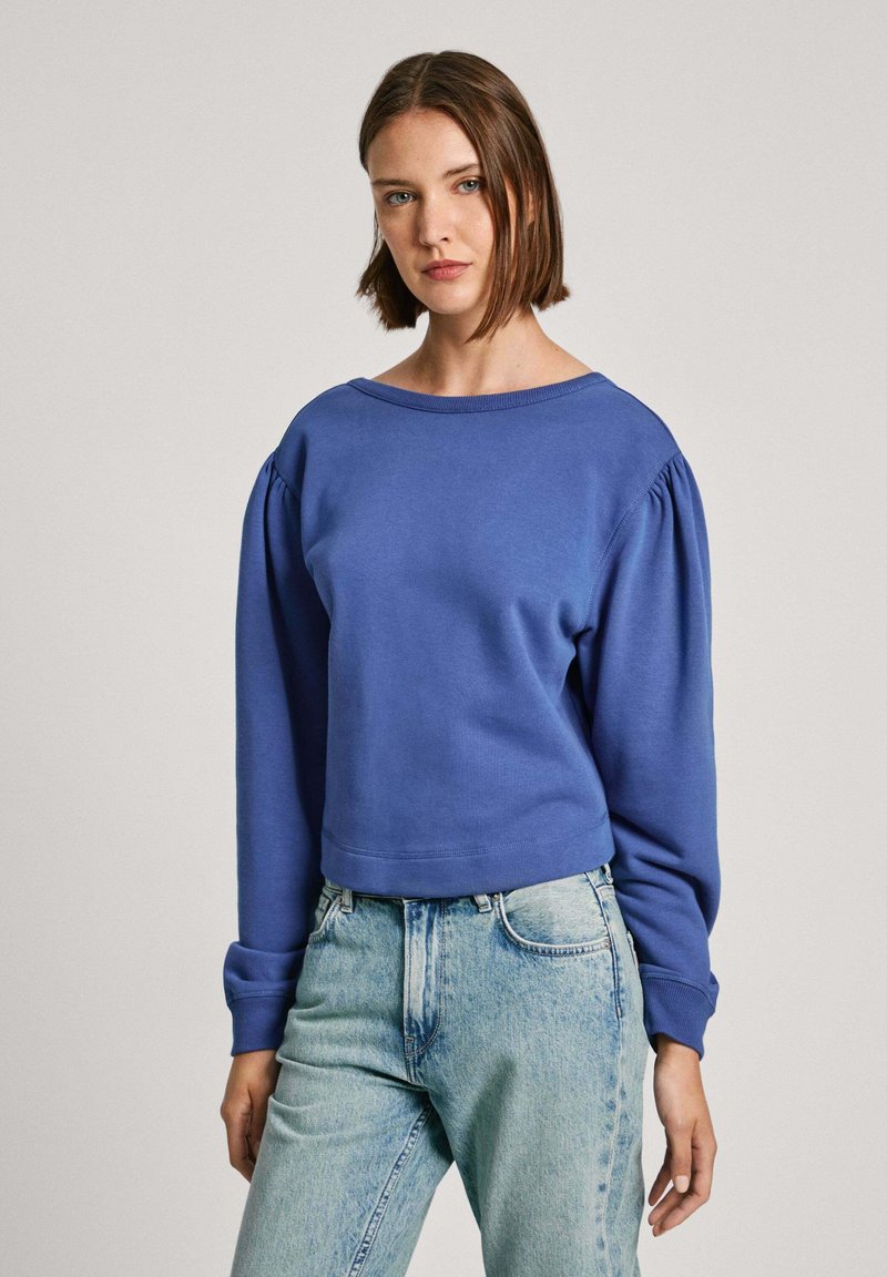 Blauw cropped sweatshirt met een brede halslijn en pofmouwen, gecombineerd met lichtgewassen denim jeans. Zachte stof, gladde textuur.