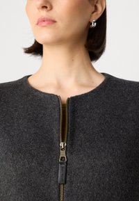 Czarna bluza zapinana na zamek, wykonana z materiału filcowego, z okrągłym dekoltem i ozdobnym złotym zamkiem z czarną zawleczką.