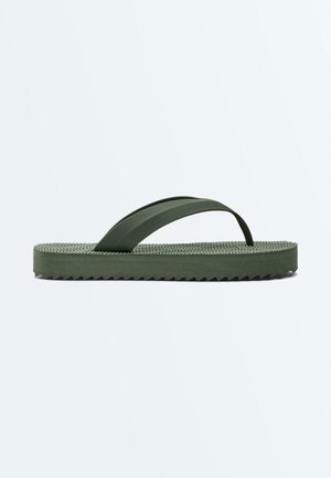 Tongs en caoutchouc vert avec semelle texturée et large bride, vues de côté sur un fond clair uni.