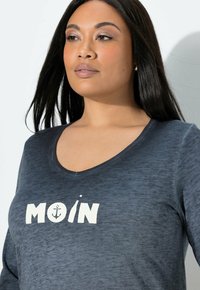 Koszula z długim rękawem w kolorze granatowym, z dekoltem w kształcie litery U i białym napisem „MOIN” oraz wzorem kotwicy. Miękki, strukturalny materiał.