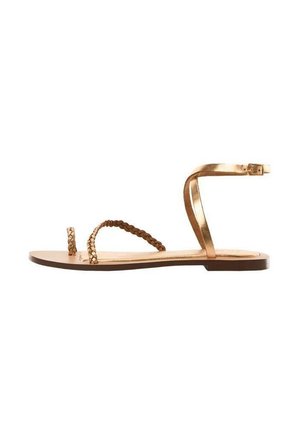 Płaska sandałka z metalicznymi złotymi paskami, z plecioną pętlą na palce i paskiem wokół kostki z zapięciem na klamrę na brązowej podeszwie.