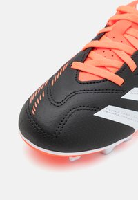 Svart fotballsko med en syntetisk, teksturert overdel, med oransje detaljer og snøring. Inkluderer hvite striper og en gummisåle.