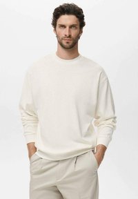 White cotton sweatshirt with long sleeves and a crew neck, paired with light beige trousers. Soft texture, relaxed fit, simple design.