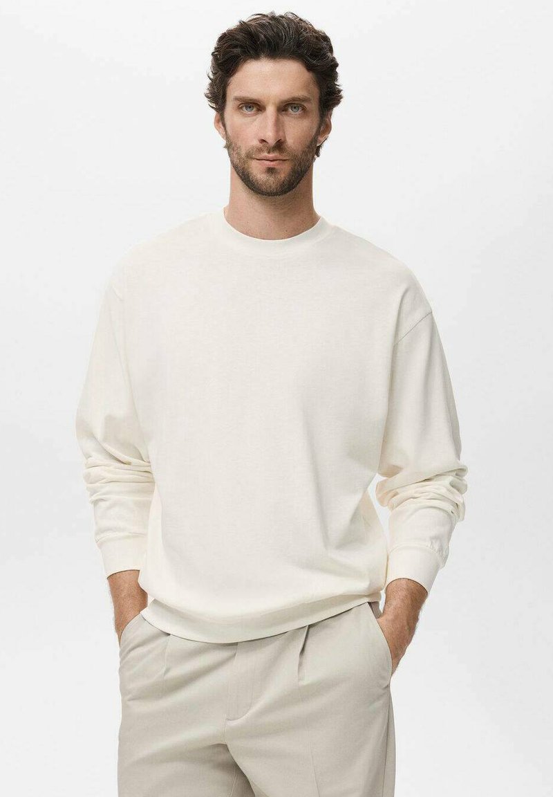 White cotton sweatshirt with long sleeves and a crew neck, paired with light beige trousers. Soft texture, relaxed fit, simple design.