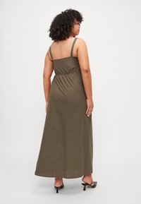 Robe maxi en vert olive, fabriquée en tissu doux. Dotée de bretelles fines et d'un corsage froncé, avec une jupe fluide et un détail au dos.