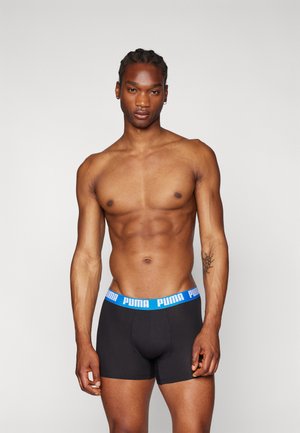 Schwarze Boxershorts mit einem blauen elastischen Bund, der mit "PUMA"-Markenlogo versehen ist. Der Stoff wirkt glatt und sitzt gut an einem männlichen Modell.