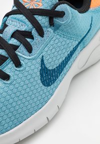 Chaussure de sport turquoise avec une tige en mesh texturé, Swoosh bleu marine, lacets noirs et accent orange. Semelle blanche avec des rainures pour l'adhérence.