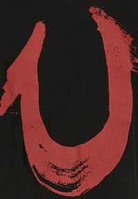 Camiseta negra con un diseño de pinceladas rojas irregulares en negrita que se asemejan al número "10" en el frontal. Textura de algodón suave.