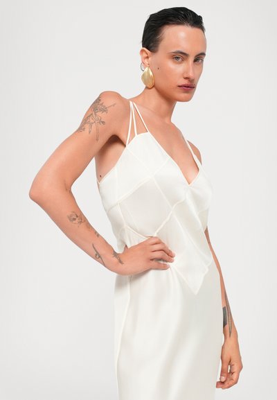 Robe blanche à bretelles spaghetti, présentant un motif géométrique et une texture lisse. Notable pour son décolleté en V profond et sa silhouette ajustée.