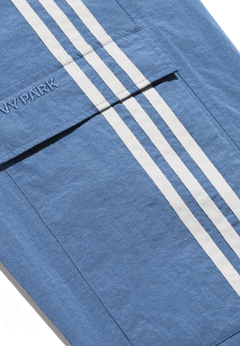 Blauwe stof met witte verticale strepen. Bevat een gestikt logo "NAVY PARK." Zachte textuur; pocketdetail zichtbaar aan de linkerkant.