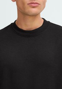 Sweatshirt nero a girocollo realizzato in tessuto morbido, con scollo a coste e superficie liscia. Nessun motivo o rifinitura visibile.