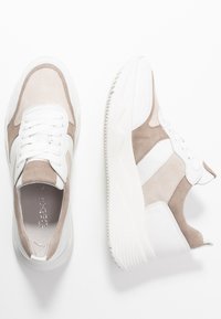 Paire de baskets en daim beige et blanc avec semelles épaisses blanches, lacets blancs et col rembourré sur fond blanc.
