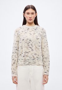 Chunky Strickpullover in Creme mit dunklen Sprenkeln. Rundhalsausschnitt und lange Ärmel mit gerippten Bündchen. Weiche Textur und lockere Passform.