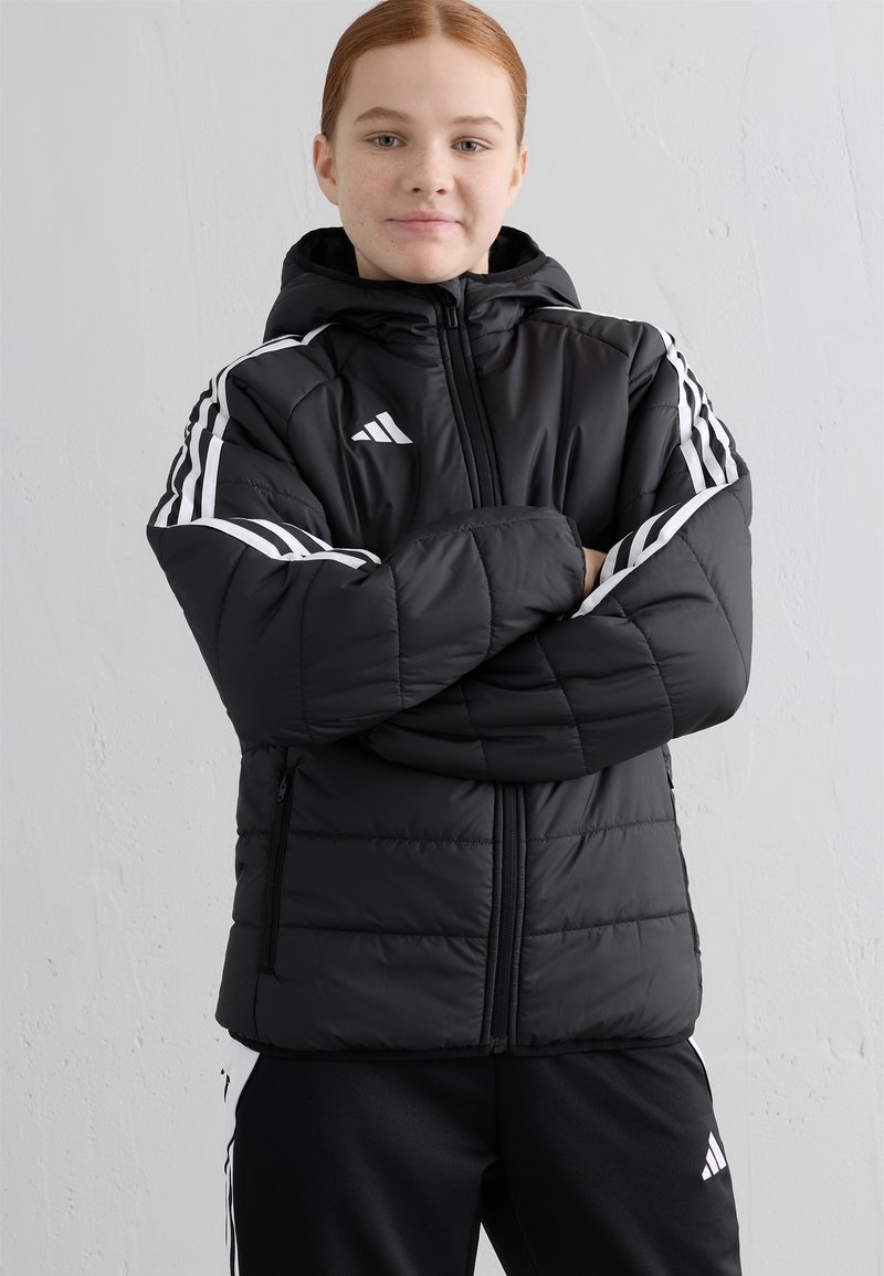 Svart pufferjakke med hette, med hvite striper langs skuldrene, glidelås og to sidelommer. Strukturert, quiltet materiale.