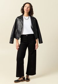 Mustahdynnah nahkaläkkärijakki, jossa on vetoketjuja, yhdistettynä valkoiseen t-paitaan, mustiin leveälahkeisiin housuihin ja mustiin matalan koron kenkiin.