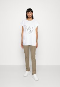 Camiseta blanca de manga corta con un dibujo de rostros en línea continua en el frontal, combinada con pantalones beige y zapatillas blancas.