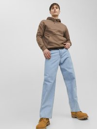 Bruine capuchontrui, lichtblauwe recht gesneden jeans en tan werklaarzen. Glad materiaal, ruime voorzak en comfortabele pasvorm.