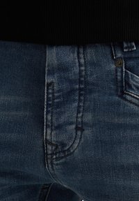Traperice u srednje plavoj boji s izblijedjelim završetkom. Imaju prednju džepu, kontrastne šavove i klasičan dizajn s pet džepova.