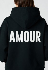 Felpa nera con cappuccio caratterizzata da una grande scritta ricamata in bianco "AMOUR" sulla schiena; vestibilità comoda con finitura testurizzata e maniche ampie.
