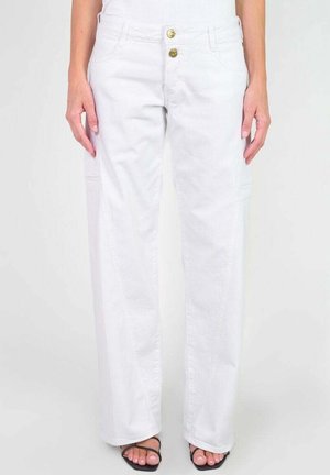 Persona vistiendo pantalones blancos de pierna ancha y talle alto con doble botón dorado y sandalias negras de tiras, de pie con las manos relajadas a los lados.