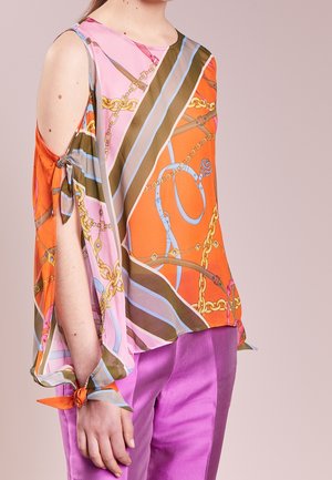 Blouse en soie colorée avec des motifs oranges, roses et bruns, agrémentée de motifs en chaîne. Comprend une découpe à l'épaule et un détail de manche nouée.