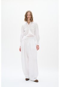 Weiße Leinenbluse mit Puffärmeln, V-Ausschnitt und Stickereidetails; kombiniert mit weißen, weiten Hosen und Ballerinas im Leopardenmuster.